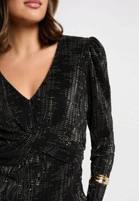 Vestito in velluto nero con strisce verticali, accenti metallici, scollo a V profondo e vita arricciata. Presenta maniche a sbuffo e un bracciale d'oro.