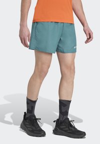 Men's teal athletic shorts with side pockets, paired with black shoes and patterned gray socks. Features a fitted design and lightweight material.