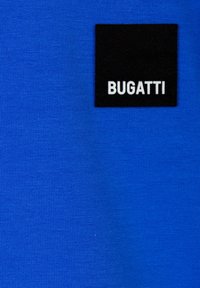 Tessuto blu con una superficie liscia, caratterizzato da un'etichetta quadrata nera con il testo bianco "BUGATTI" cucito su un lato.