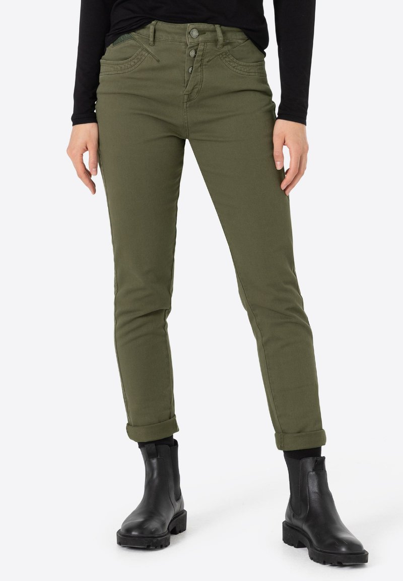 Olijfgroene, getailleerde broek met een medium hoge taille, vijf-pocket ontwerp, opgerolde manchetten en metalen knopen. Gecombineerd met zwarte enkellaarzen.