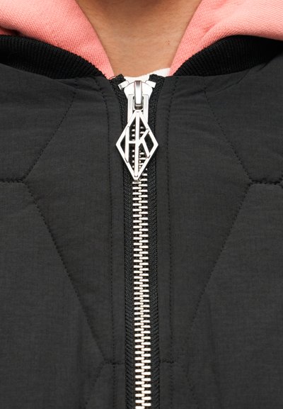 Μαύρο καπιτονέ μπουφάν με αντίθετη ροζ κουκούλα. Διαθέτει ασημένιο φερμουάρ με τριγωνικό έλκτη, που αναδεικνύει υφή από ελαφρύ ύφασμα.