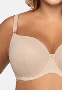 Soutien-gorge rembourré beige avec des cups lisses, une bordure en dentelle décorative et un accent de nœud central. Bretelles réglables et fermeture à crochets.
