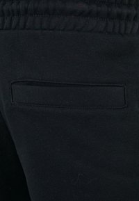 Black cotton fabric featuring a smooth texture with a stitched pocket detail on the back. The waistband is gathered for comfort.