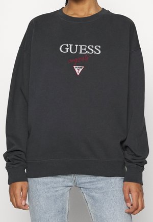 Sudadera gris oscuro con puños y dobladillo acanalados, que presenta bordados de texto "GUESS" y "originals", detalle de logotipo triangular en el pecho.