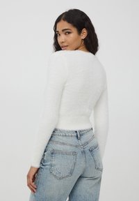 Maglione bianco fluffoso con maniche lunghe e una vestibilità aderente, abbinato a jeans a vita alta in denim chiaro con tasche posteriori.