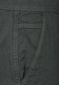 Mörkgrått tyg med ett fiskbensmönster, med en framficka och kontrasterande sömmar längs kanterna. Texturerad yta synlig.