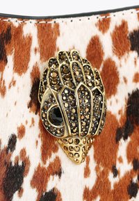 Tessuto animale marrone e bianco con un ornamento decorativo a forma di conchiglia color oro, impreziosito da strass neri e trasparenti.