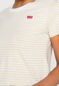 Pasek t-shirt w jasnych kolorach, z białym okrągłym dekoltem i małym czerwonym logiem Levi's na piersi, wykonany z miękkiej tkaniny.
