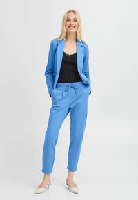 Light blue blazer and matching jogger set in soft fabric. Black lace camisole underneath. White pointed-toe shoes as accents.