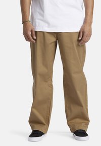 Khaki bukser lavet af bomuld, med en afslappet pasform og lige ben design. Båret med en hvid skjorte og sorte sneakers.