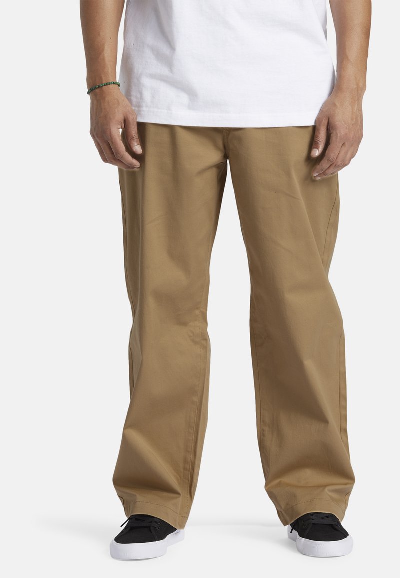 Khaki bukser lavet af bomuld, med en afslappet pasform og lige ben design. Båret med en hvid skjorte og sorte sneakers.