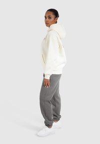 Felpa bianca con una grande tasca, maniche a coste e cappuccio regolabile, abbinata a pantaloni della tuta grigi e sneakers bianche.