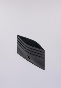 Portafoglio in pelle nera con tre slot per carte e un compartimento centrale, posizionato su uno sfondo grigio chiaro uniforme.