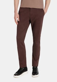 Brązowe bawełniane spodnie o slim fit, charakteryzujące się gładką fakturą i klasycznymi kieszeniami, w połączeniu z czarnymi trampkami.