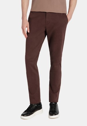 Brązowe bawełniane spodnie o slim fit, charakteryzujące się gładką fakturą i klasycznymi kieszeniami, w połączeniu z czarnymi trampkami.