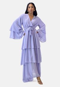 Abito a strati color lavanda con maniche lunghe a campana e cintura annodata in vita. Realizzato in tessuto leggero, presenta una silhouette fluida e una texture semi-trasparente.