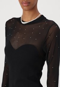 Black long-sleeve top with sheer fabric dotted with small silver accents, featuring a sweetheart neckline and ribbed lower panel.