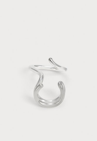 Une bague manchette ouverte en argent poli, composée de bandes courbes fluides qui se chevauchent, sur un fond clair uni.
