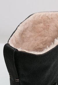 Zwarte enkellaars met een zachte, lichtroze imitatiebont voering, leren buitenkant, afgeronde vorm en contrasterende stiksels langs de rand.