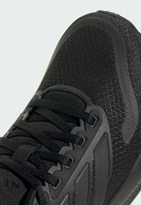 Baskets de sport noires en matériaux en maille et synthétiques, surface texturée, embout renforcé, lacets plats et semelle à motif.