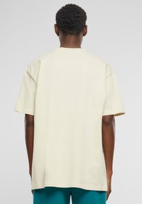 Lys beige kortærmet t-shirt lavet af blødt stof, med en afslappet pasform, rund halsudskæring og lige søm, vist fra bagsiden.