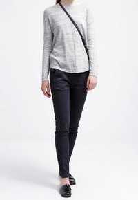 Lichtgrijs longsleeve shirt met een ronde hals, zwarte slim-fit broek en zwarte platte schoenen met een glanzende afwerking. Eenvoudig ontwerp, geen patronen.