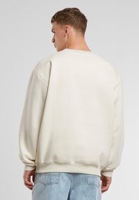 Cremefarvet oversized sweatshirt med ribbet kant og manchetter, med round hals og sænkede skuldre, lavet af blødt stof.