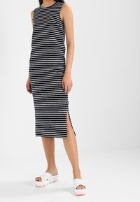 Abito senza maniche a righe in bianco e nero, con spacchi laterali e una forma dritta. Abbinato a sandali con plateau bianchi e suole rosa.