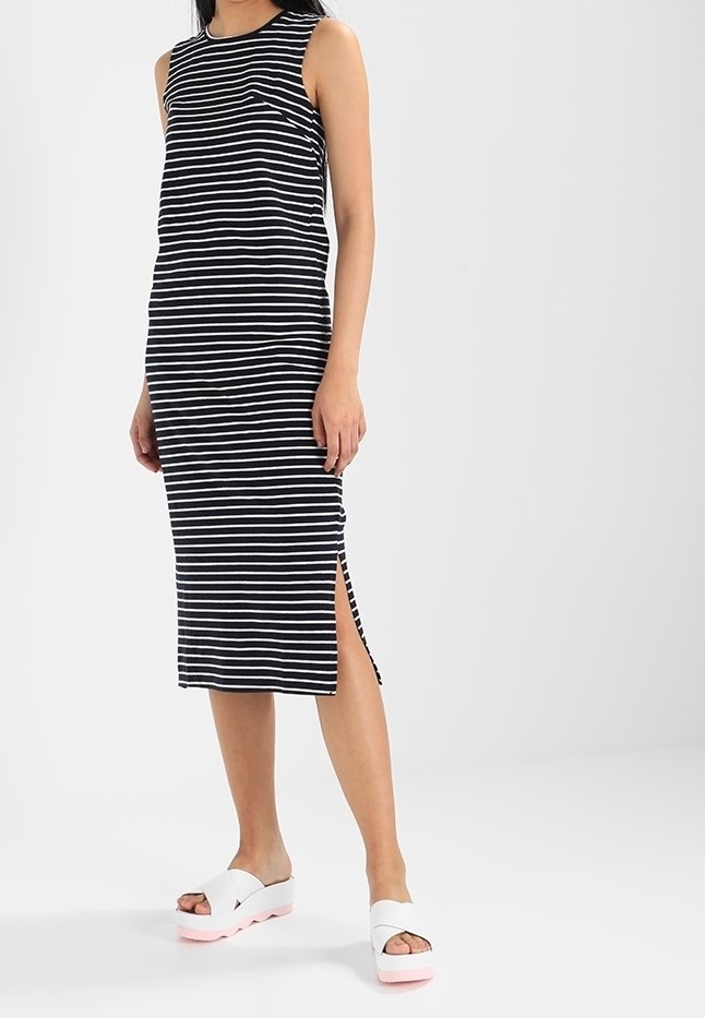 Czarna i biała, w paski, bezrękawnikowa sukienka z bocznymi rozcięciami i prostym krojem. Połączona z białymi sandałami na platformie z różowymi podeszwami.