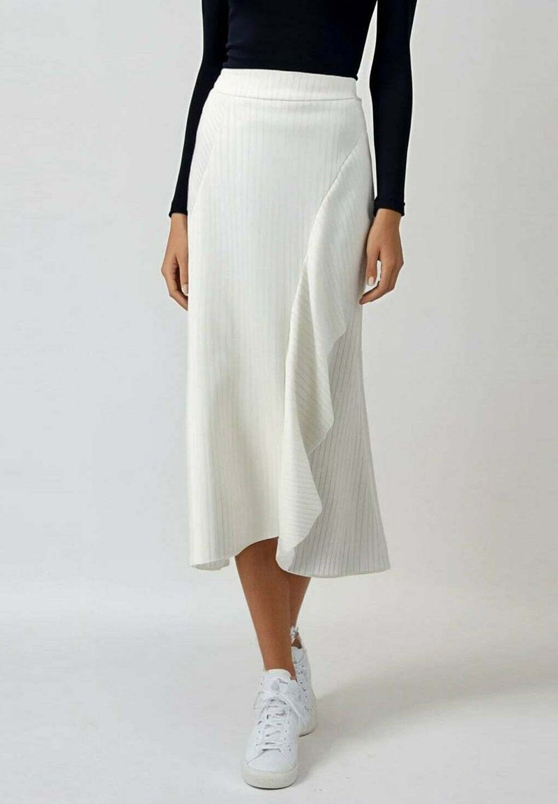 Jupe midi blanche à côtes avec un ourlet ondulé, associée à des baskets blanches, présentant une taille ajustée et une texture subtile.