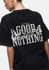 Czarny, oversize t-shirt z białym napisem graficznym "PRESENTED BY GOOD FOR NOTHING" oraz ilustracjami motyli na plecach. Materiał bawełniany.