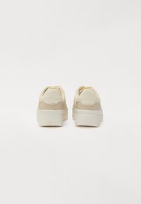 Sneakers z kremowym wierzchem, beżowymi akcentami, teksturowaną skórą i zamszem oraz grubą białą gumową podeszwą.