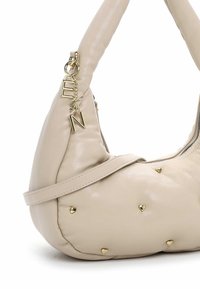 Borsa beige con un design morbido e imbottito, caratterizzata da borchie a forma di cuore dorate e una catena dorata con ciondoli a lettere. Texture liscia e tracolla regolabile.