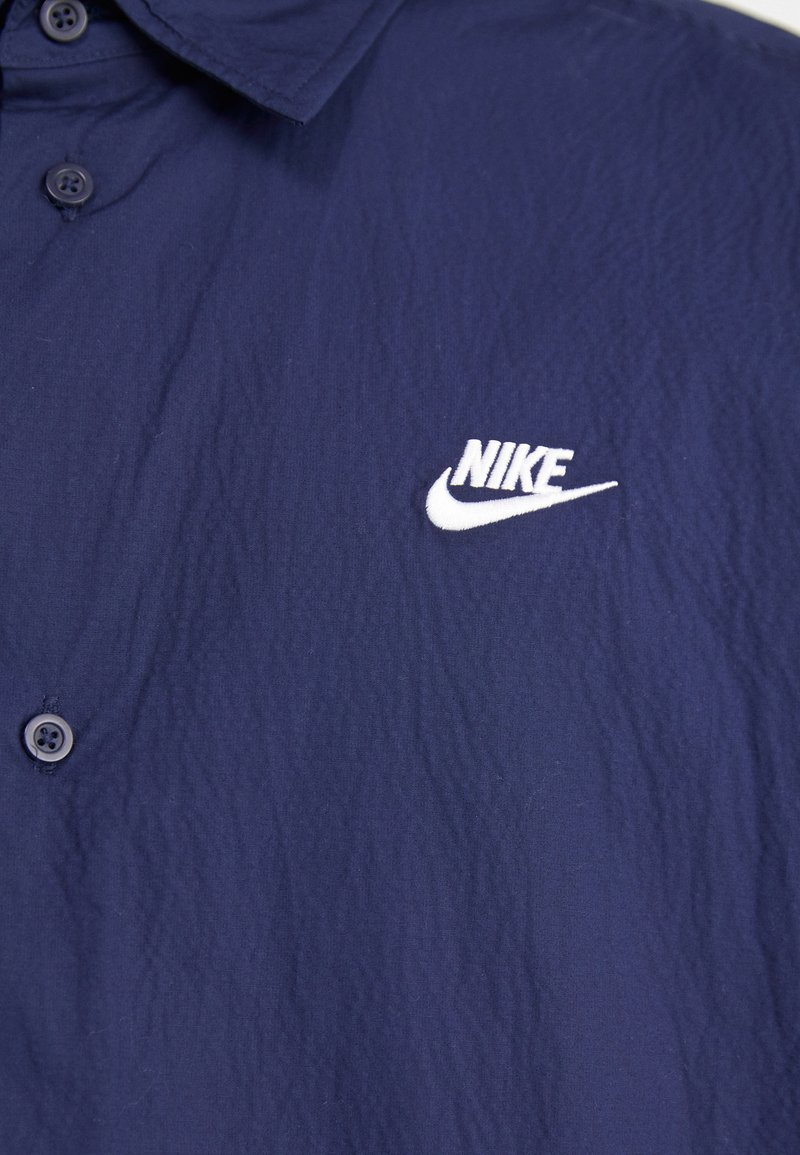 Polo shirt Nike bleu marine en tissu texturé, avec un col boutonné et un logo brodé blanc sur la poitrine gauche.
