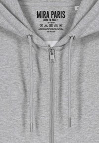 Felpa grigia con zip realizzata in 100% cotone. Caratterizzata da una zip YKK, cordini e un'etichetta stampata con il nome del brand e le istruzioni per il lavaggio.