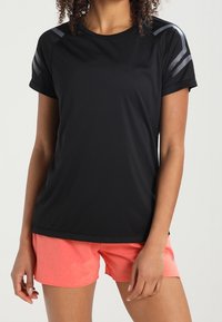 Camiseta deportiva negra de manga corta con detalles estampados en gris en los hombros, combinada con pantalones cortos color coral en un tejido suave y texturizado.