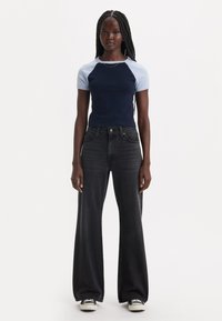 T-shirt ajusté bicolore bleu marine et bleu clair associé à un jean noir taille haute et large. Porté avec des baskets blanches.
