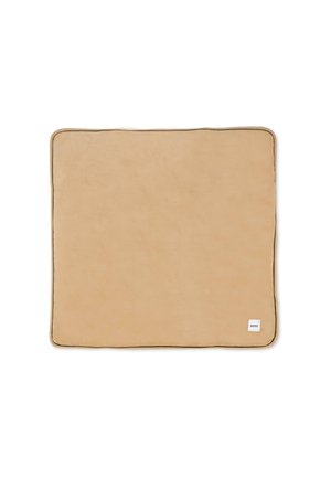 Couverture rectangulaire beige avec une texture douce, terminée par un bord contrastant foncé. Présente une petite étiquette blanche dans le coin inférieur.