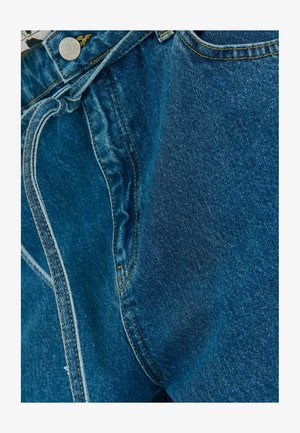 Pantalones de mezclilla en azul medio con costuras visibles, cierre de botón y cordón. Presenta bordes de bolsillo y una textura suave.