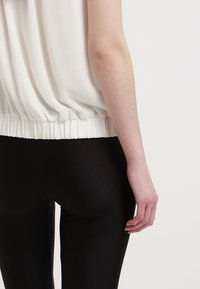 Haut ample crème avec ourlet froncé, associé à des leggings noirs ajustés ; texture de tissu lisse et détails de design simples.