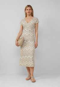 Abito beige con motivo a zigzag, maniche corte, scollatura a V e lunghezza fino al polpaccio. Abbinato a una borsa beige e sandali con cinturini.