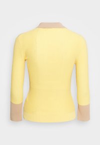 Pull jaune côtelé à manches longues avec col beige et poignets beiges, vu de dos sur un fond blanc uni.