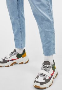 Paksupohjaiset tennarit, joissa yhdistyvät useat materiaalit; harmaat, valkoiset, vihreät, keltaiset ja punaiset yksityiskohdat; kuviolliset päälliset; ja paksu valkoinen pohja.