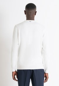 Maglione bianco lavorato a maglia con maniche lunghe, collo rotondo e orlo a costine. Tessuto morbido, design minimale con dettaglio di cucitura sul retro. Abbinato a pantaloni scuri.
