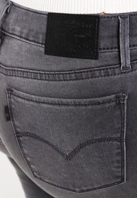 Jeans in denim grigio con etichetta in pelle nera, caratterizzati da un design della tasca posteriore curva. Texture liscia con dettagli di cucitura a contrasto.