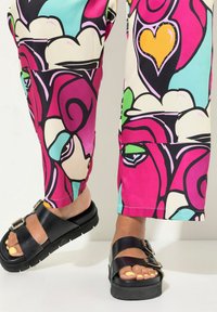 Zwarte platform sandalen met dubbele banden en gespen, gecombineerd met levendige roze, groene en turquoise gestreepte broek met abstracte ontwerpen.