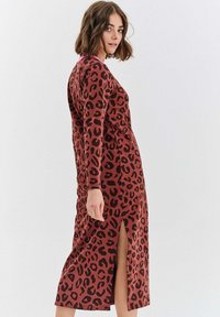 Hnědé šaty s leopardím potiskem a dlouhými rukávy, s bočním rozparkem, s přiléhavým střihem a měkkou texturou. Minimalistický styl, žádné viditelné kování.