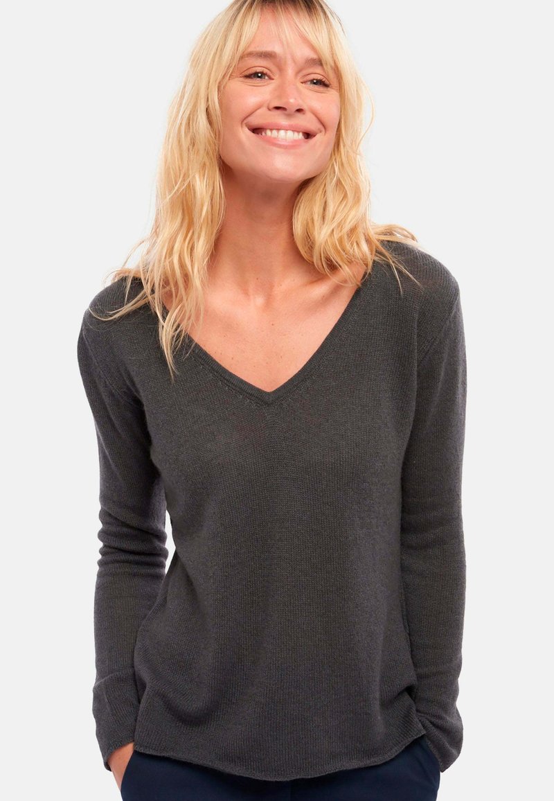 Dunkelgrauer, gerippter Strickpullover mit V-Ausschnitt und langen Ärmeln, entspannter Schnitt und subtiler Textur, präsentiert an einem Model vor einem schlichten Hintergrund.