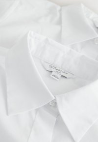 Chemises à col blanc, tissu lisse, design net, fermeture à boutons et détails cousus ; un col légèrement chevauchant l'autre.