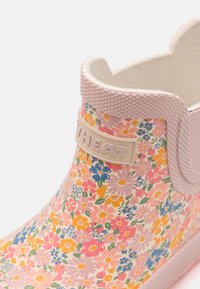 Rosa gummistøvel med blomsterdesign til ankelen, med en strukturert mansjett og merkebånd. Glatte, fargerike blomster i ulike størrelser dekker overflaten.